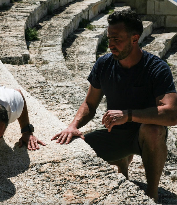 Coach demonstrating a controlled squat pattern to an older client