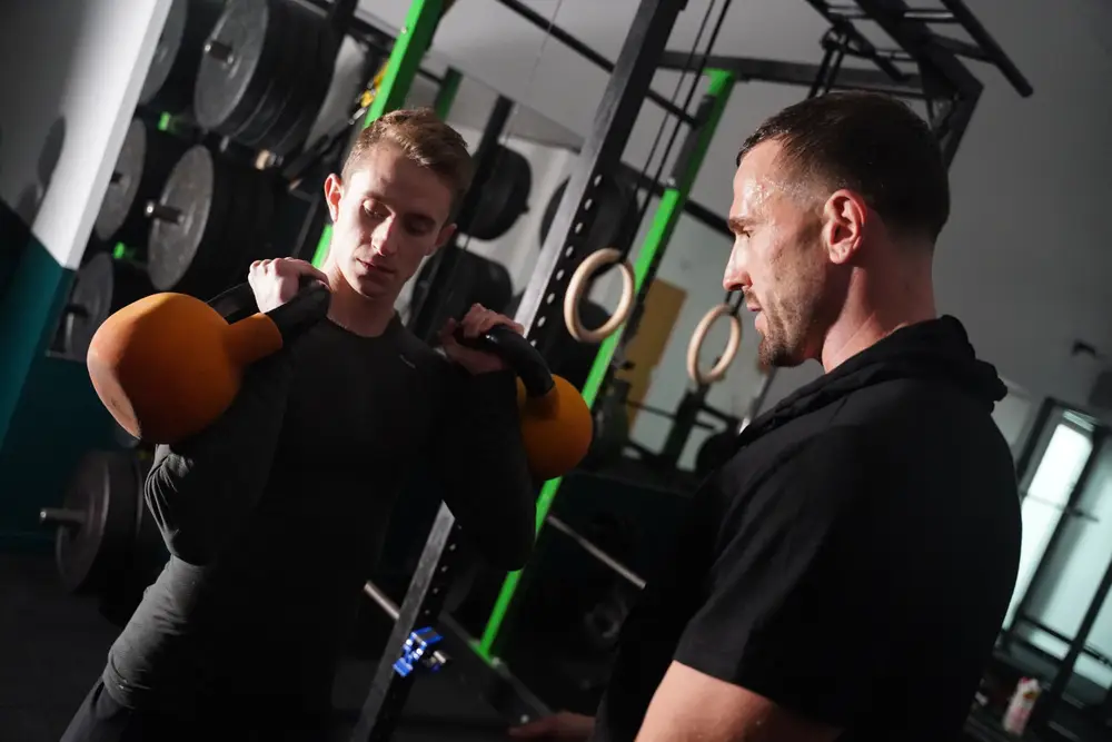 Personal trainer coaching a client through a kettlebell lift in a Cambridge gym